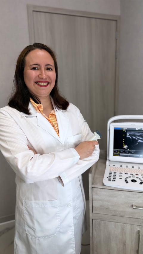Female healthcare professional in white lab coat and striped shirt smiling next to ultrasound machine in medical office
